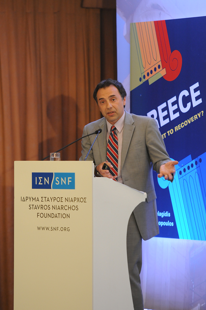 Ένας άντρας μιλά στο βήμα του Ιδρύματος Σταύρος Νιάρχος και πίσω του υπάρχει ένα banner το οποίο γράφει GREECE FROM EXIT TO RECOVERY?