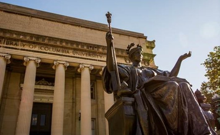 Φωτογραφία ενός χάλκινου αγάλματος μιας γυναίκας που διαβάζει ένα βιβλίο με τα χέρια απλωμένα έξω από τη Βιβλιοθήκη του Columbia University