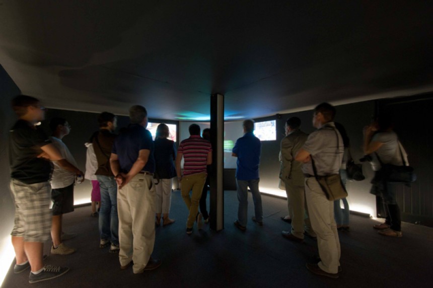 Μια ομάδα ανθρώπων βρίσκονται σε μια αίθουσα και παρακολουθούν τις οθόνες που υπάρχουν στον χώρο