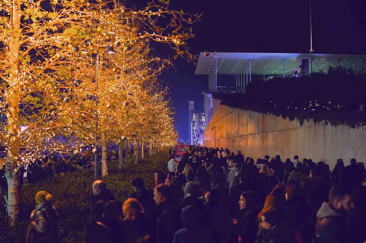 Πλήθος ανθρώπων κοιτάζει τα χριστουγεννιάτικα στολισμένα δέντρα μπροστά από μια λίμνη 