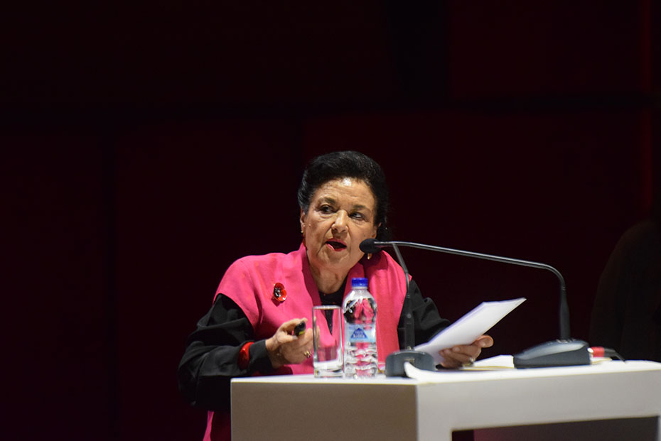 Μια γυναίκα κρατάει χαρτιά και εκφωνεί ομιλία στη σκηνή