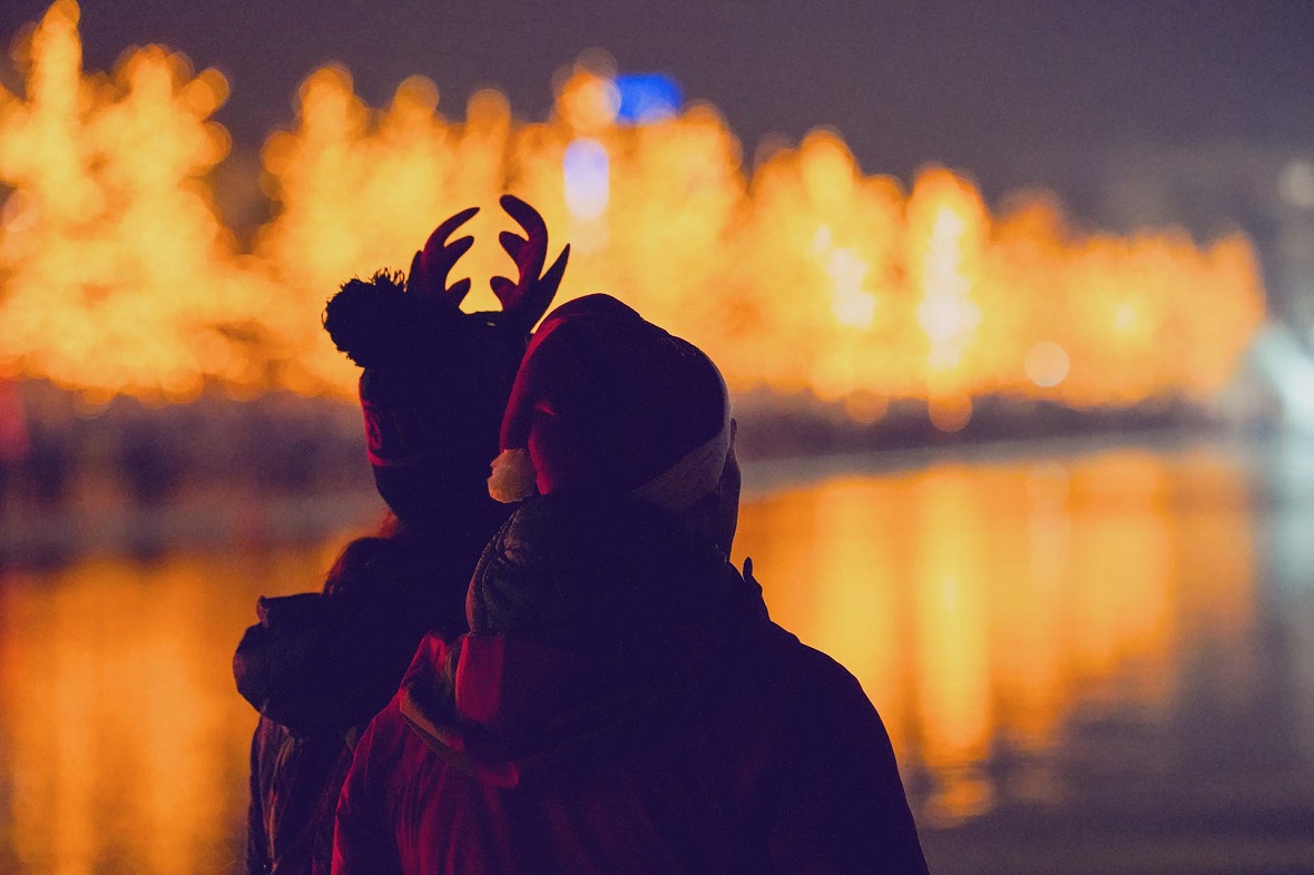 Δύο φίλοι κοιτάνε μια λίμνη και φοράνε χριστουγεννιάτικους σκούφους 