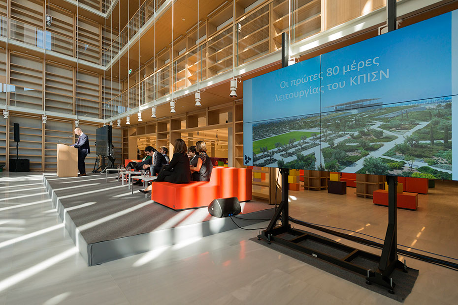 Ένας άνδρας μιλάει σε ένα βήμα στην Εθνική Βιβλιοθήκη με μια οθόνη που γράφει 