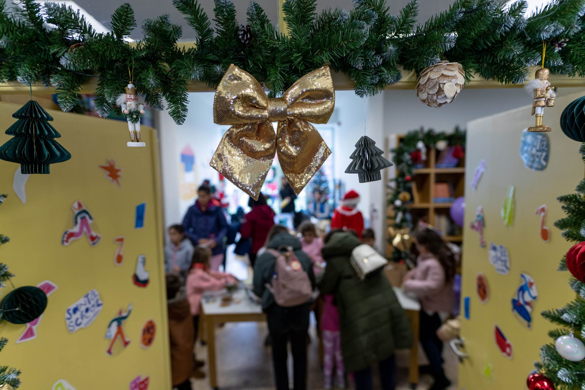 Παιδιά γύρω από ένα τραπέζι μέσα από τις πόρτες του Vamvakou Santa School, ανάμεσα σε στολίδια και αυτοκόλλητα.