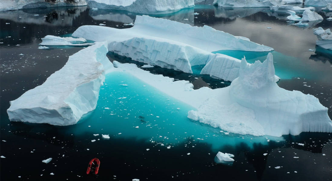 Two scuba divers are dwarfed by the iceberg they're swimming next to.