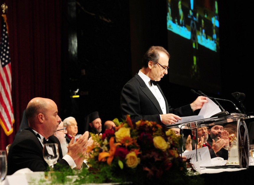 Πλαινή φωτογραφία που δείχνει ένα μέλος του Οικουμενικού Πατριαρχίου να στέκεται στο βήμα και να κοιτά τα χαρτιά που έχει μπροστά του