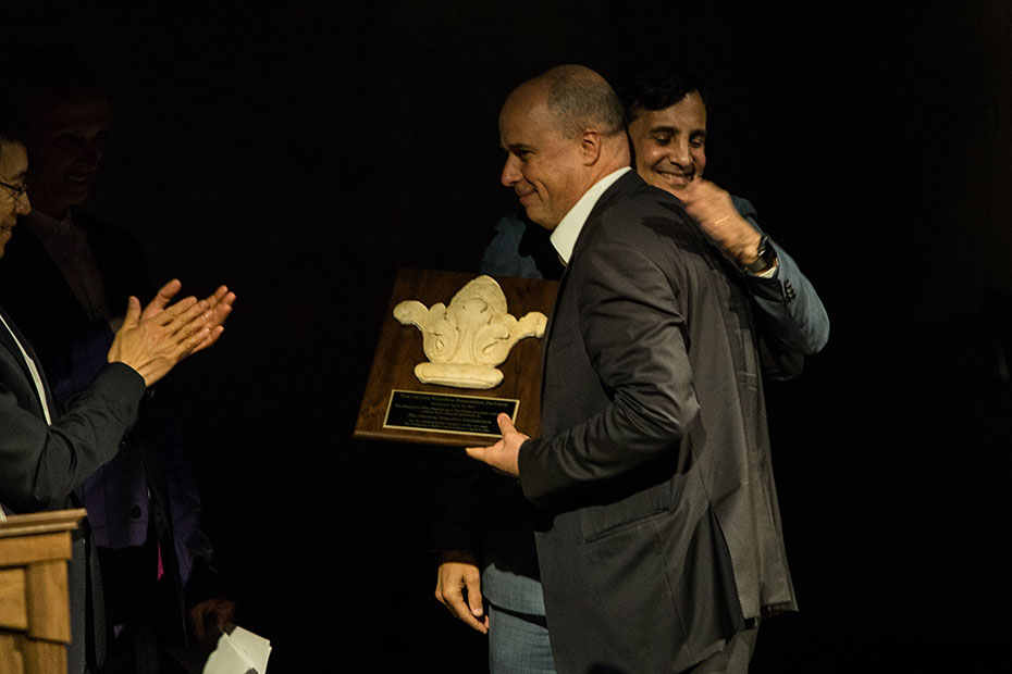 Ο Αντρέας Δρακόπουλος, Πρόεδρος του Ιδρύματος Σταύρος Νιάρχος, κρατάει ένα δώρο τιμής και ένας άντρας τον αγκαλιάζει ενώ ένας άλλος χειροκροτά