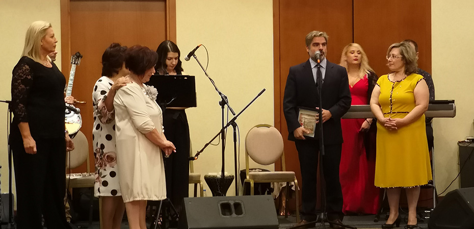 Ένας άνδρας που κρατάει ένα βραβείο μιλάει στο μικρόφωνο ενώ οι άνθρωποι γύρω του τον ακούνε