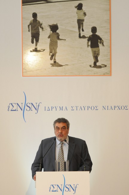 Ένας άνδρας μιλάει στη σκηνή στο Ίδρυμα Σταύρος Νιάρχος κάτω από μια εικόνα παιδιών που τρέχουν