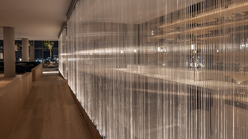 Στον εσωτερικό χώρο ενός εστιατορίου υπάρχει μια διάφανη διαχωριστική κουρτίνα φτιαγμένη από κλωστές φωτός 