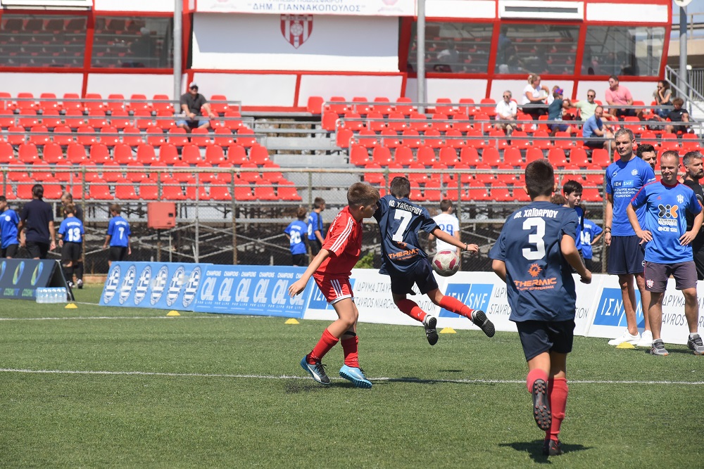 Τρια νεαρά αγόρια παίζουν ποδόσφαιρο και δύο προπονητές τους παρακολουθουν