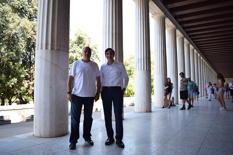 Ο Ανδρέας Δρακόπουλος και ένας άλλος άνδρας χαμογελούν μπροστά από στήλες σε αρχαιολογικό μουσείο