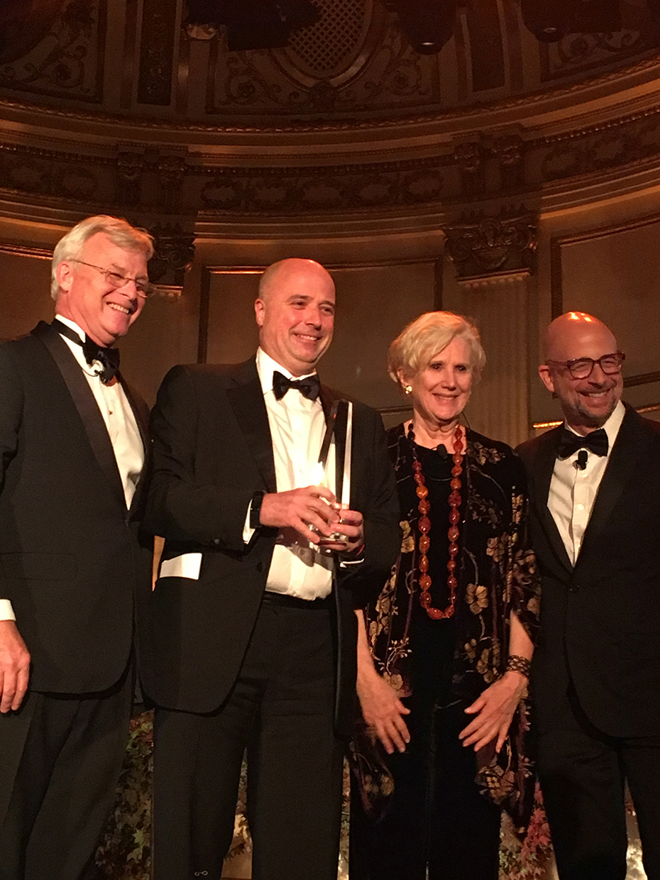 Ο Αντρέας Δρακόπουλος, Πρόεδρος του Ιδρύματος Σταύρος Νιάρχος, κρατάει ένα βραβείο τιμής και φωτογραφίζεται χαμολεστός με μία γυναίκα και δύο άντρες που στέκονται δίπλα του 