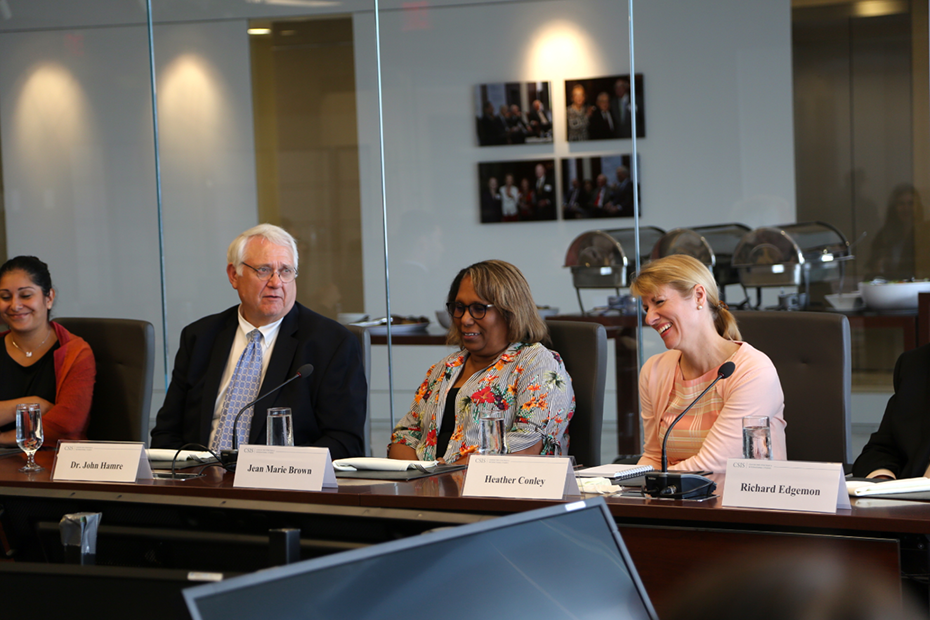 Ένας άνδρας και τρεις γυναίκες κάθονται σε ένα τραπέζι συσκέψεων με ετικέτες ονομάτων και μικρόφωνα