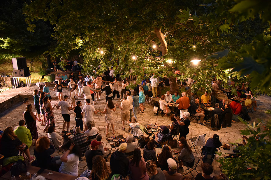 Νυχτερινή φωτογραφία που δείχνει πλήθος ανθρώπων να χορεύει και να κάθεται στην κεντρική πλατεία του χωριού