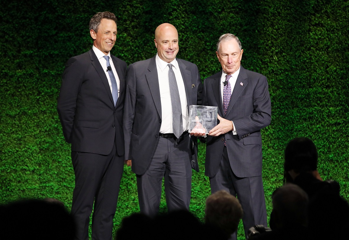 Andreas Dracopoulos, President of the Stavros Niarchos Foundation, standing with two other men holding a gift of honor and posing for a commemorative photograph 