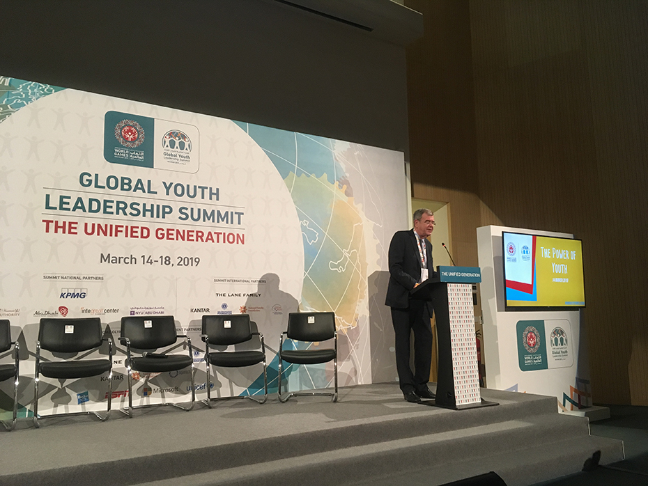 Ένας άνδρας μιλάει σε μια εξέδρα μπροστά από μια προβολή που γράφει 