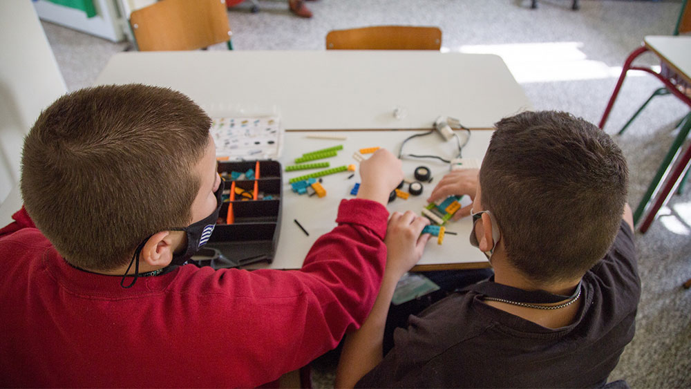 Δύο μικρά αγοράκια φοράνε μάσκα και συναρμολογούν διάφορα LEGO