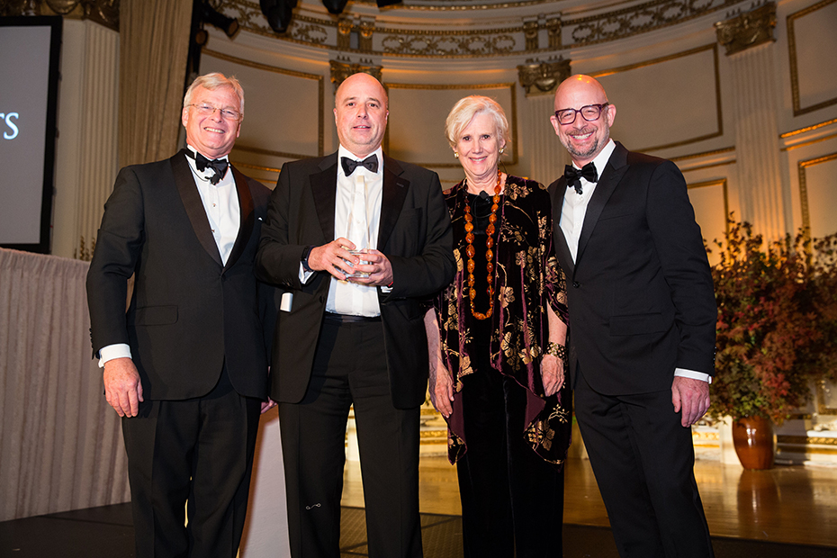 Ο Αντρέας Δρακόπουλος, Πρόεδρος του Ιδρύματος Σταύρος Νιάρχος, κρατάει ένα βραβείο τιμής και φωτογραφίζεται χαμολεστός με μία γυναίκα και δύο άντρες που στέκονται δίπλα του 