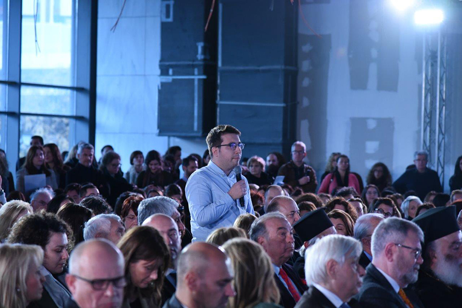 Ένας άντρας στέκεται όρθιος ανάμεσα στο κοινό και θέτει τον προβληματισμό του κρατώντας ένα μικρόφωνο