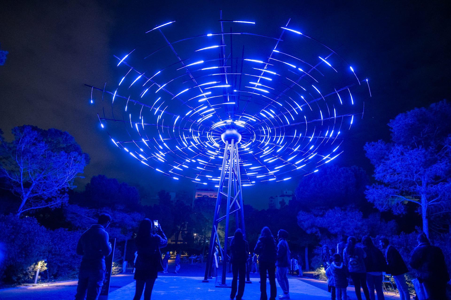 Άνθρωποι συγκεντρωμένοι γύρω από μια μεγάλη μπλε φωτιστική εγκατάσταση.