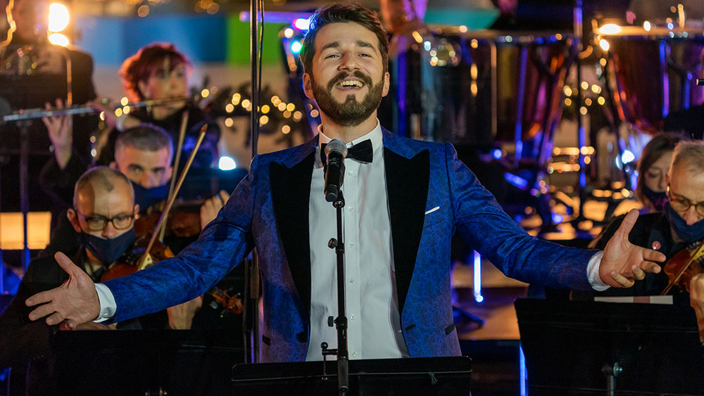 Ένας άνδρας τραγουδάει χαμογελώντας μπροστά σε μια ορχήστρα