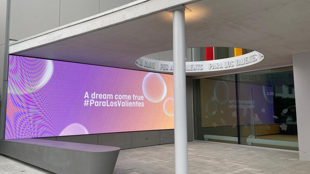 Μια φωτογραφία του λόμπι στο Παιδιατρικό Κέντρο Καρκίνου στο Νοσοκομείο Παίδων Sant Joan de Déu στη Βαρκελώνη, όπου μια μεγάλη οθόνη προβάλλει την επιγραφή 