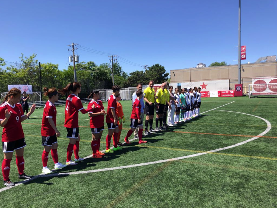 Σε ένα γήπεδο ποδοσφαίρου στη γραμμή του κέντρου στέκονται δυο γυναικείες ποδοσφιαιρκές ομάδες και ανάμεσά τους δύο διαιτητές