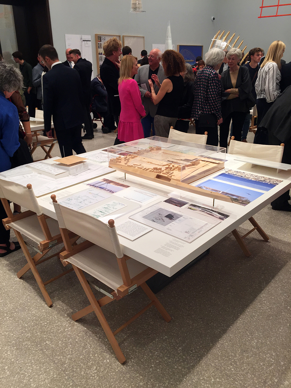 Κοντινή φωτογραφία από ένα τετράγωνο τραπέζι πάνω στο οποίο υπάρχουν μακέτες και περιγραφές κτηρίων 