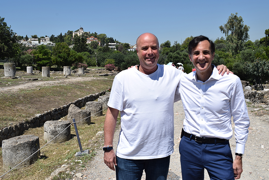 Ο Ανδρέας Δρακόπουλος και ένας άλλος άνδρας χαμογελούν και βγάζουν μια φωτογραφία μπροστά από έναν αρχαιολογικό χώρο