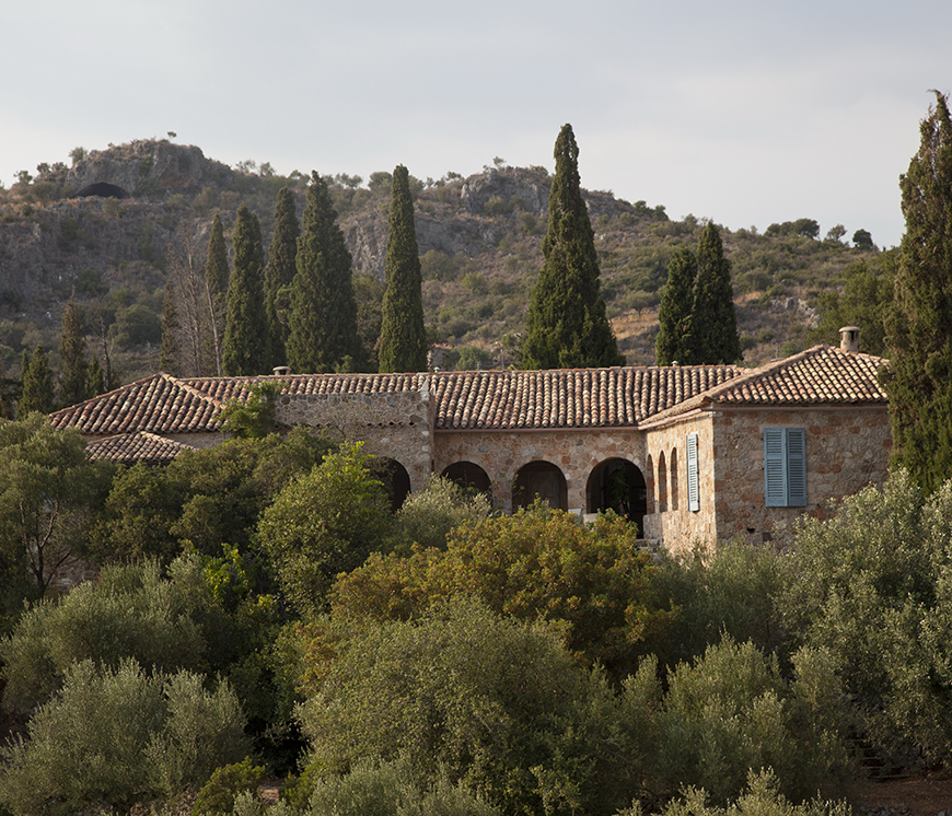 Φωτογραφία που δείχνει ένα πέτρινο οίκιμα να ξεπροβάλει ανάμεσα στα δέντρα σε ένα βουνό 
