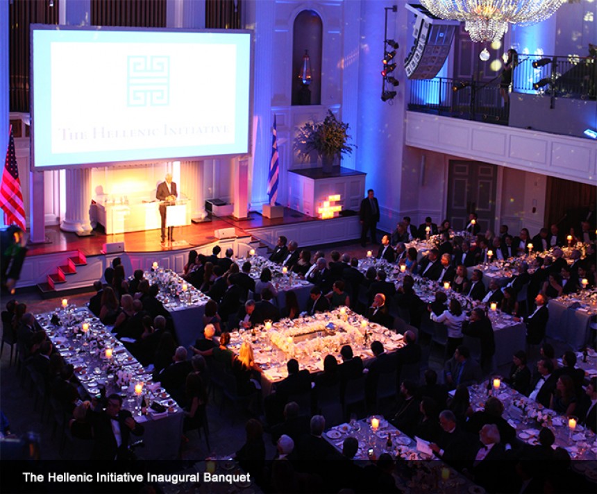 Φωτογραφία τραβηγμένη από ψηλά η οποία δείχνει πλήθος κόσμου να κάθεται σε τετράγωνα τραπέζια και να παρακολουθούν μια ομιλία