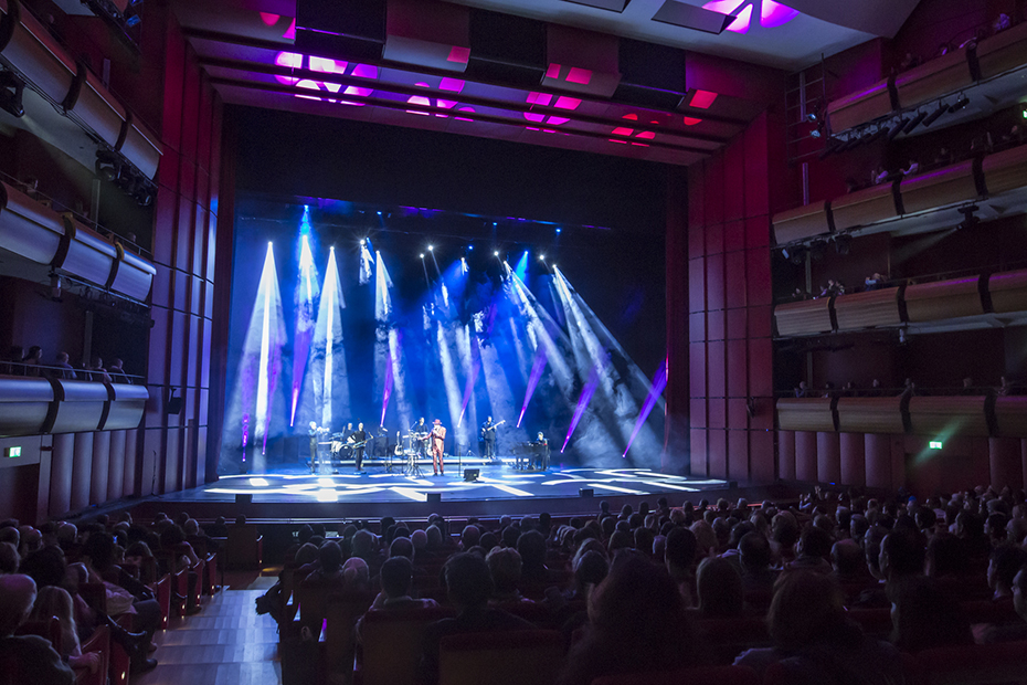 Ένα καθισμένο πλήθος παρακολουθεί μια ζωντανή μπαντα στη σκηνή της Εθνικής Λυρικής Σκηνής