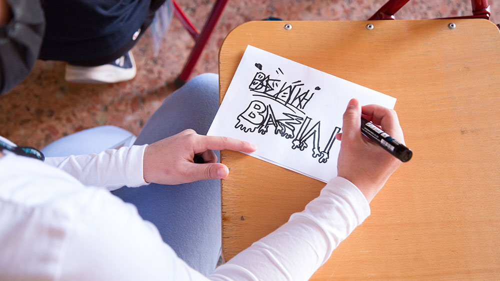 Μια κοπέλα γράφει σε ένα χαρτί το όνομά της με διάφορους τρόπους σαν graffiti