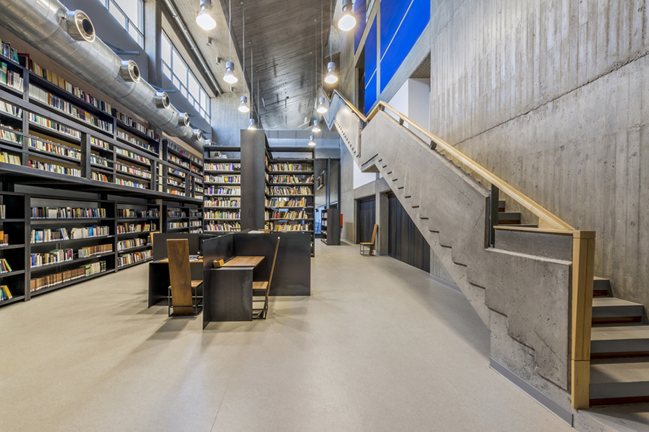 Φωτογραφία που δείχνει τον εσωτερικό χώρο μιας βιβλιοθήκης στον οποίο υπάρχουν ράφια γεμάτα βιβλία, τρπέζια με καρέκλες και μια σκάλα που οδηγεί σε άλλον όροφο 
