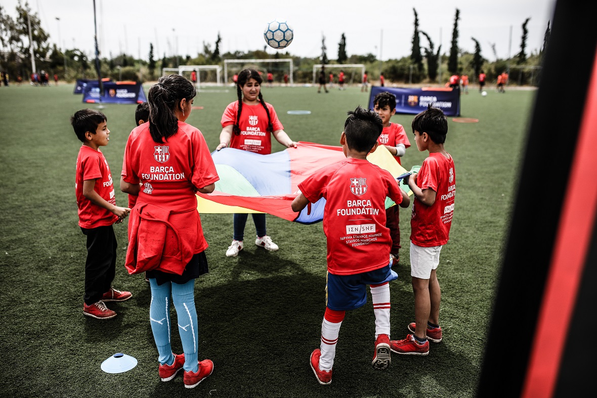Επτά παιδιά κρατούν ένα πολύχρωμο σεντόνι και πετούν μια μπάλα σε αυτό