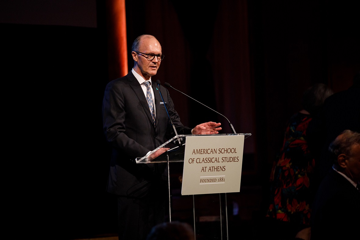 A man gives a speech on a podium with a sign that writes 