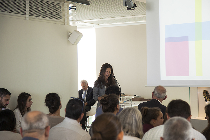 Μια γυναίκα βγάζει λόγο στο βήμα και το κοινό από κάτω την παρακολουθεί