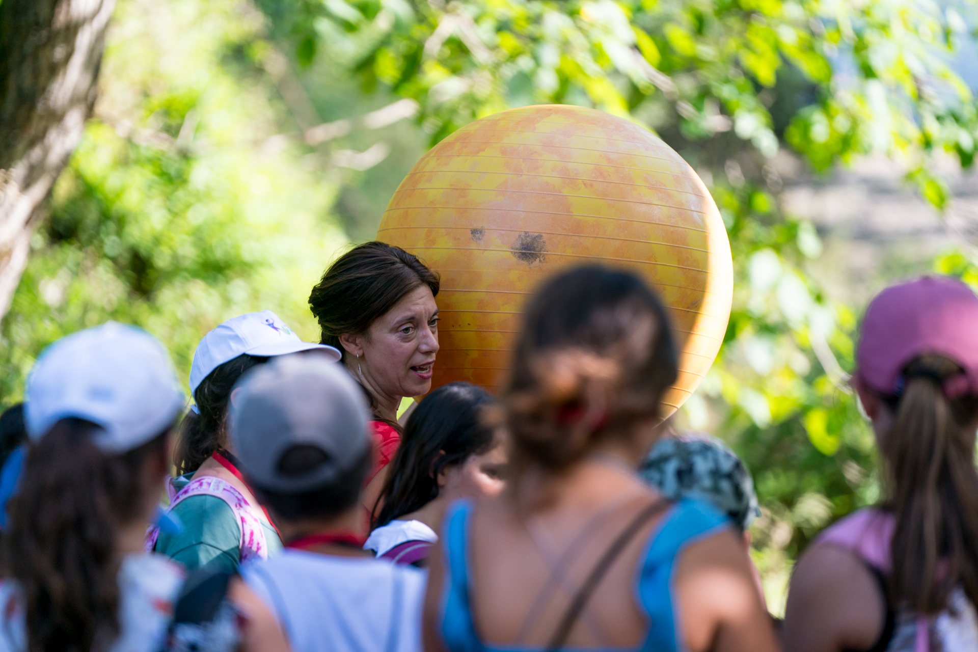 Μια γυναίκα σηκώνει μια μεγάλη μπάλα γυμναστικής μπροστά σε μια ομάδα παιδιών 
