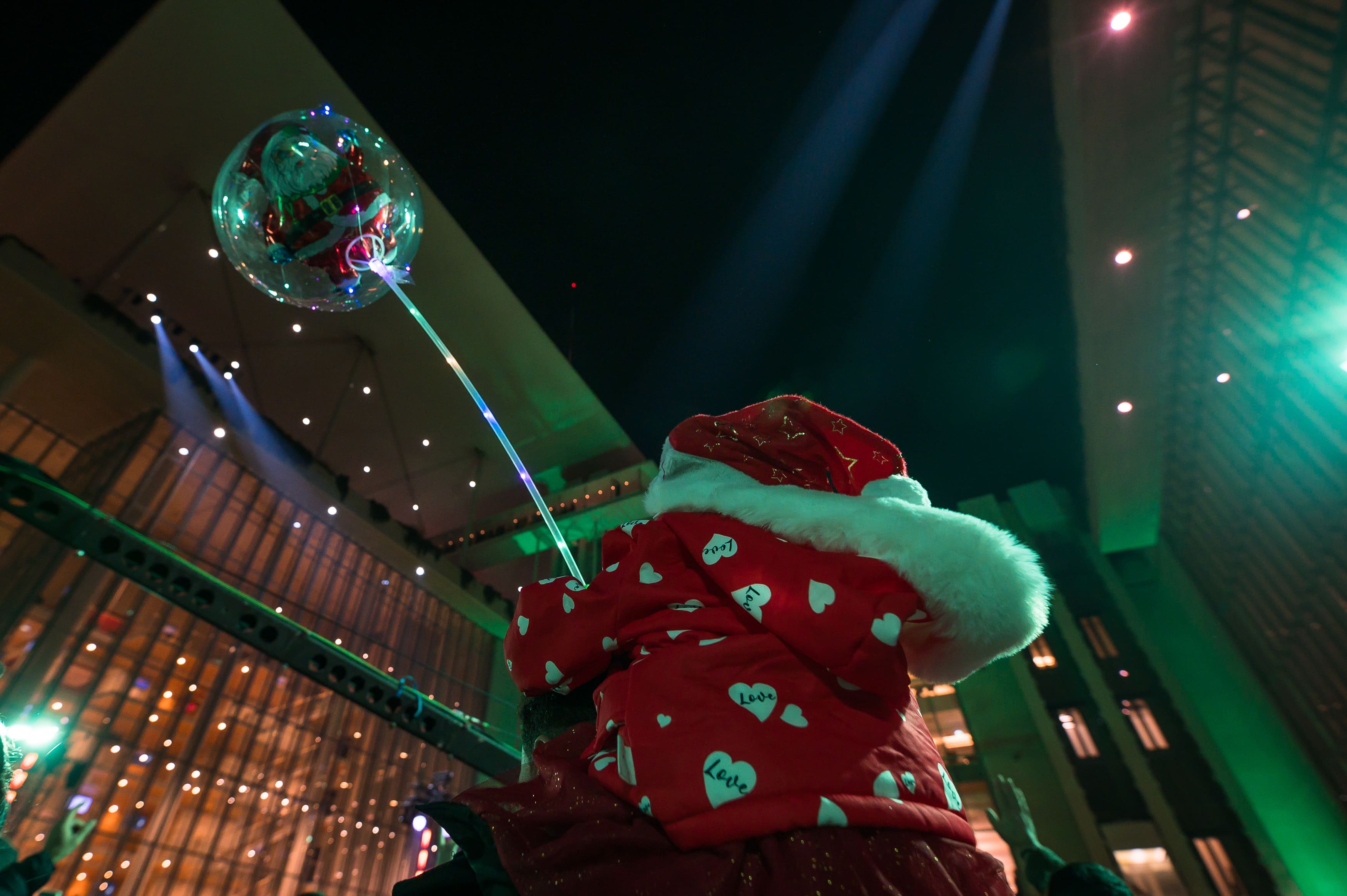 Ένα παιδί ντυμένο με χριστουγεννιάτικο σκούφο, κρατώντας ένα μπαλόνι στην Αγορά του ΚΠΙΣΝ.