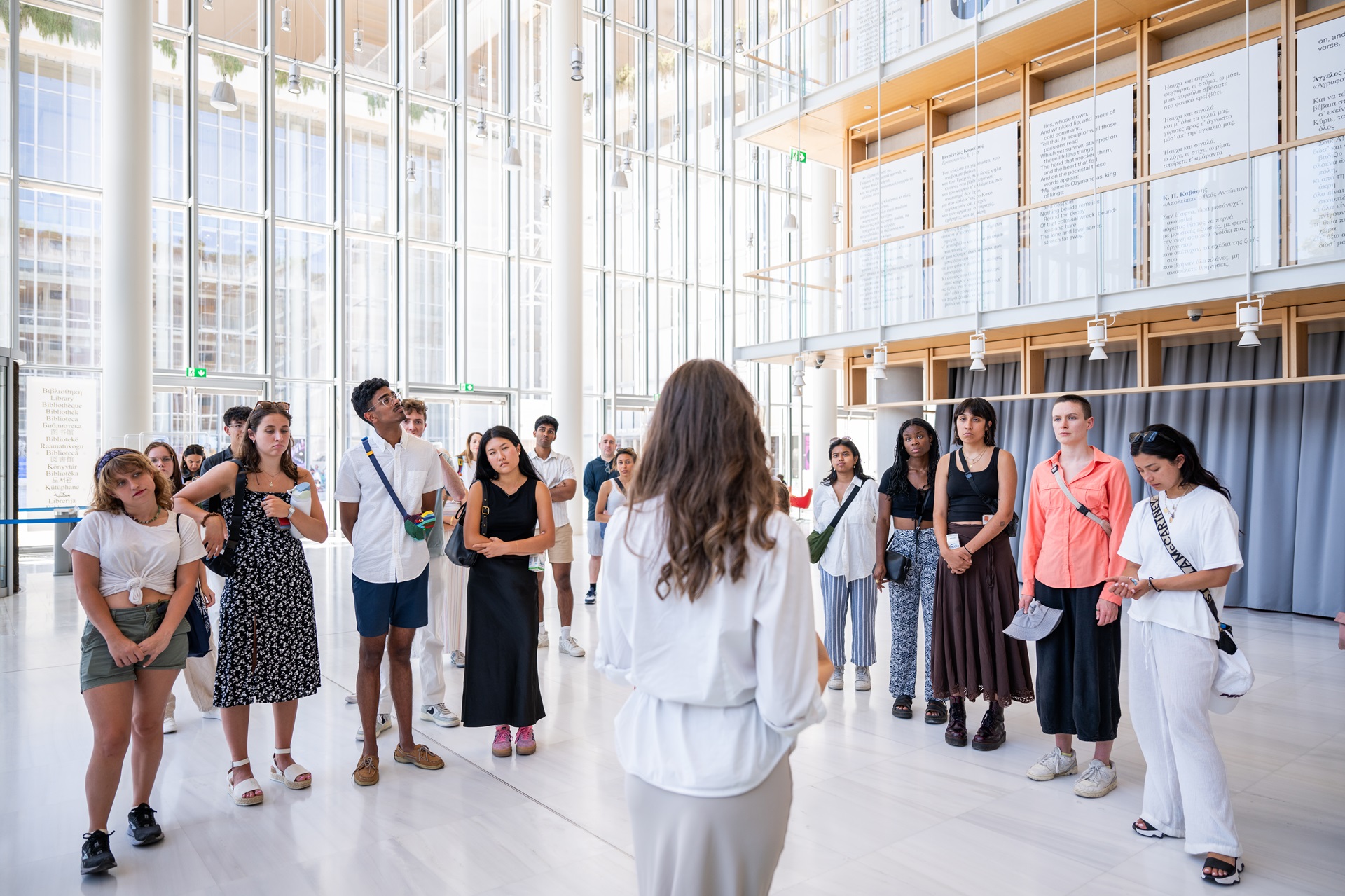 Οι επισκέπτες συγκεντρωμένοι σε κύκλο γύρω από τον ξεναγό στην Εθνική Βιβλιοθήκη της Ελλάδας.