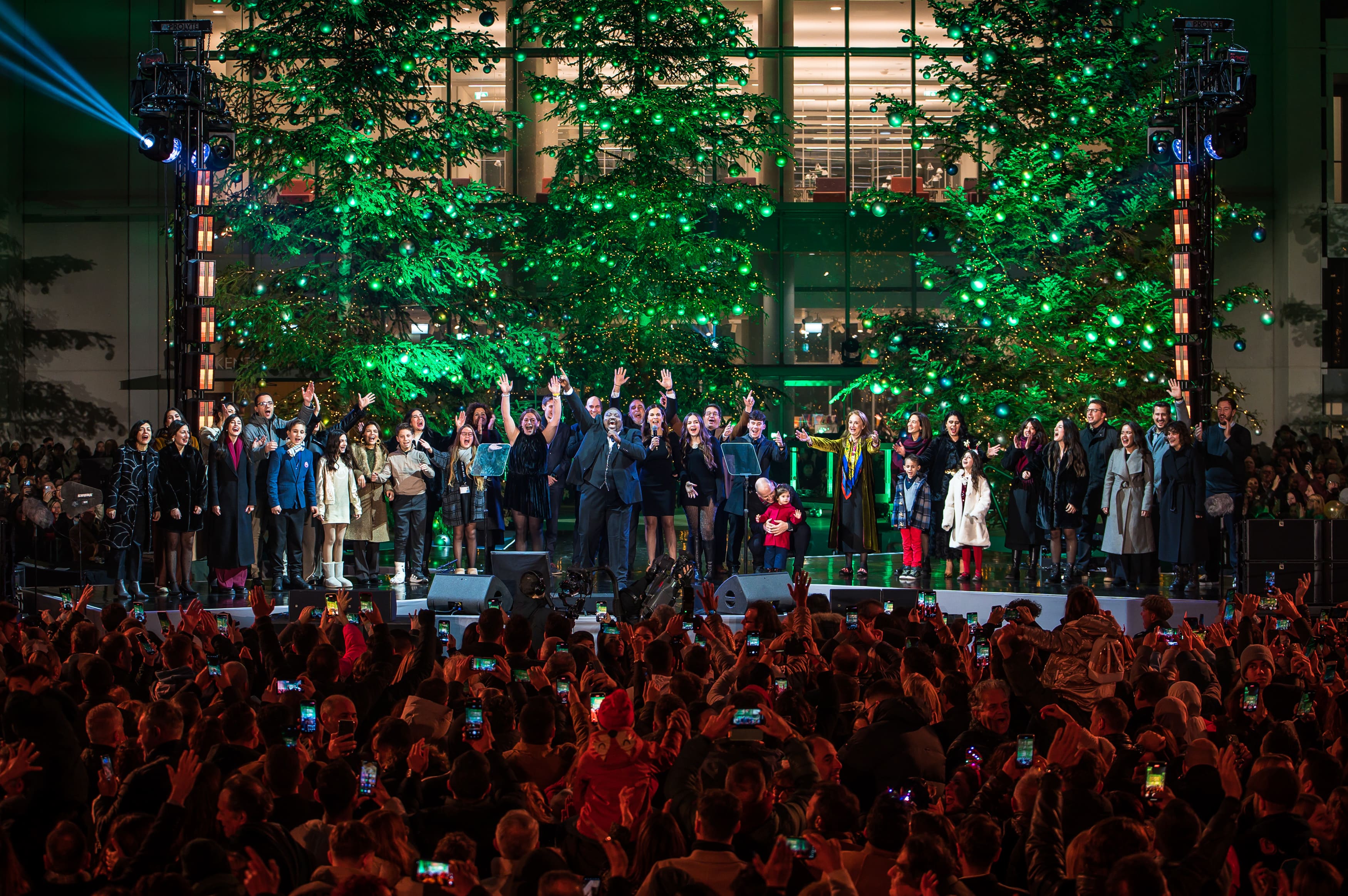 Ένα πλήθος ατόμων πάνω στη σκηνή του ΚΠΙΣΝ μετρώντας αντίστροφα με το κοινό, μπροστά από χριστουγεννιάτικα δέντρα.