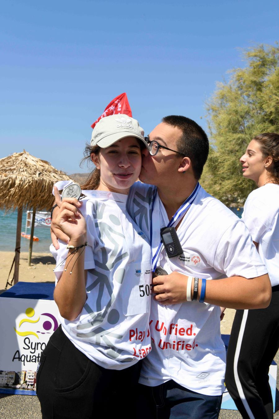 Ένας νεαρός άνδρας και ένα νεαρό κορίτσι αγκαλιάζονται και κρατούν τα μετάλλια των Special Olympics Hellas