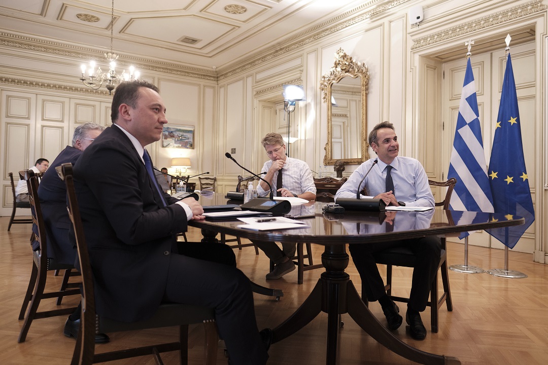 Φωτογραφία του Κυριάκου Μητσοτάκη, Πρωθυπουργού της χώρας να κάθεται σε ένα τραπέζι μαζί με άλλους άντρες και να παρακολουθούν μια σύσκεψη 