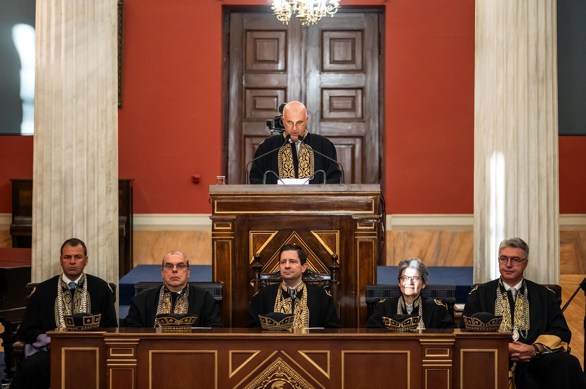 Ο Καθηγητής Παύλος Μυριανθεύς στέκεται όρθιος στο βήμα, ντυμένος με τήβεννο, κατά την ανάγνωση των κειμένων του Ψηφίσματος των Τμημάτων Ιατρικής και Νοσηλευτικής της Σχολής Επιστημών Υγείας.