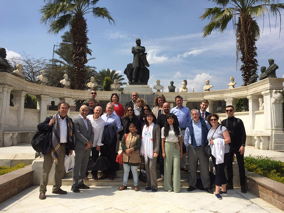 Μια ομάδα ανθρώπων στέκονται για μια αναμνηστική φωτογραφία και πίσω τους υπάρχει ένα αμφιθεατρικό τοίχος με προτομές