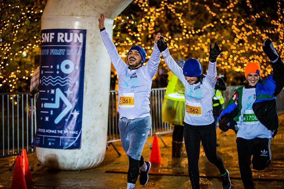 Τρεις άνθρωποι σηκώνουν τα χέρια τους από χαρά καθώς περνούν τη γραμμή τερματισμού του SNF RUN