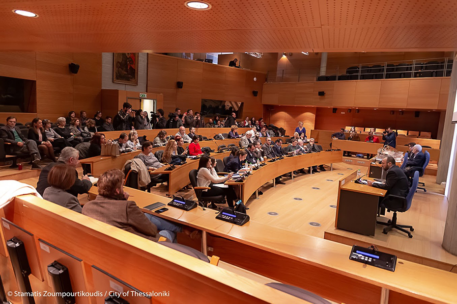 Φωτογραφία που δείχνει ένα συνεδριακό χώρο στον οποίο υπάρχουν έδρανα για τους συμμετέχοντες και μια σκηνή με έδρανα για τους ομιλητές/παρουσιαστές