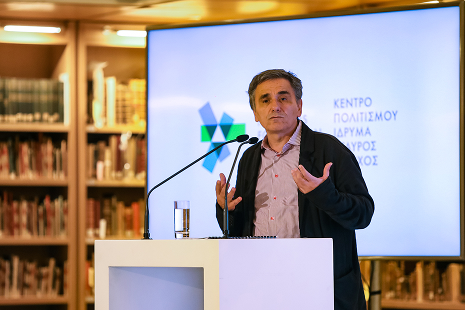 Ένας άντρας στέκεται στο βήμα και μιλάει ενώ πίσω του προβάλλεται μια φωτογραφία η οποία γράφει ΚΕΝΤΡΟ ΠΟΛΙΤΙΣΜΟΥ ΙΔΡΥΜΑ ΣΤΑΥΡΟΣ ΝΙΑΡΧΟΣ