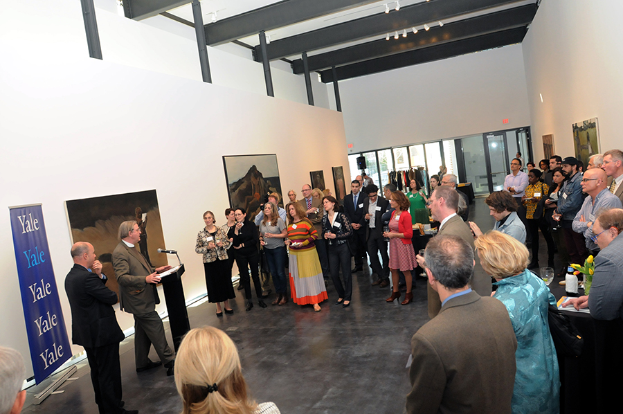 Μακρινή φωτογραφία που δείχνει έναν άντρα να μιλάει στο βήμα και δίπλα του να στέκεται ο Αντρέας Δρακόπουλος, Πρόεδρος του Ιδρύματος Σταύρος Νιάρχος και το κοινό να στέκεται και να τους παρακολουθεί 